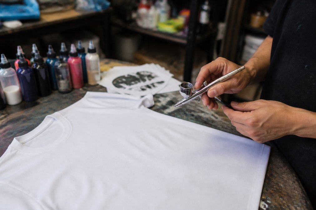 Step-by-step process of using a custom airbrush tool to create designs on a plain white cotton t-shirt