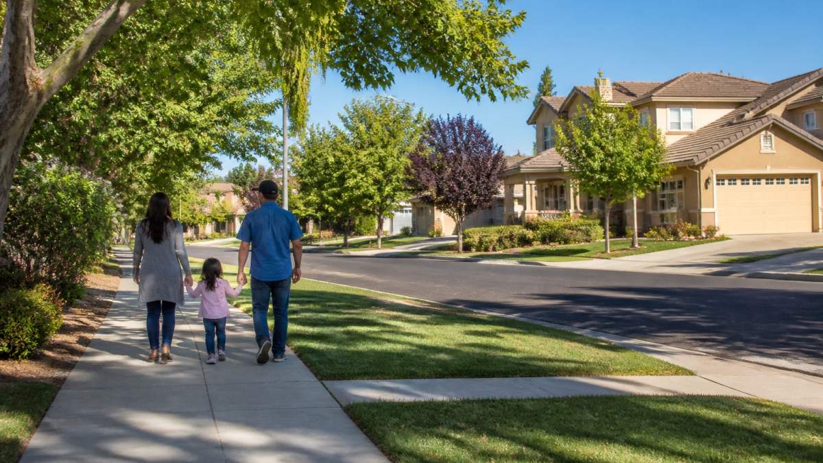 Tree-lined residential street in a Merced County neighborhood with single-family homes, well-maintained yards, and families walking together on a sunny afternoon