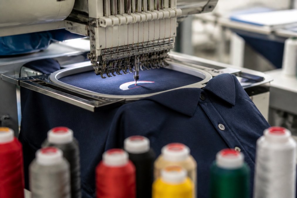 Commercial embroidery machine stitching a company logo onto navy bulk workwear polo shirts in a bright workshop