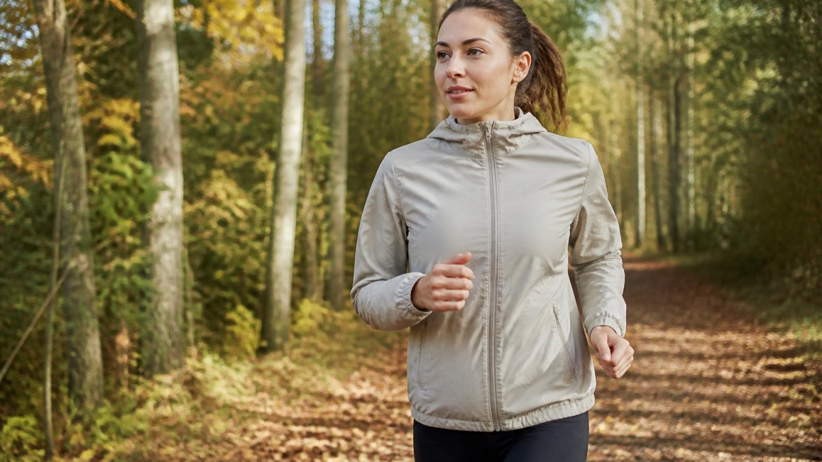 Joggerin in einer Funktionsjacke aus Naturfasern auf einem herbstlichen Waldweg bei Tageslicht.