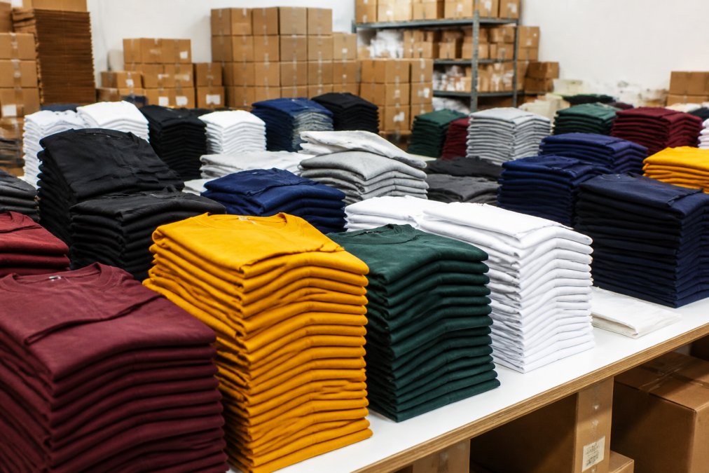 Production facility with organized stacks of custom printed apparel in various colors ready for shipment, showing professional packaging and scale of operations