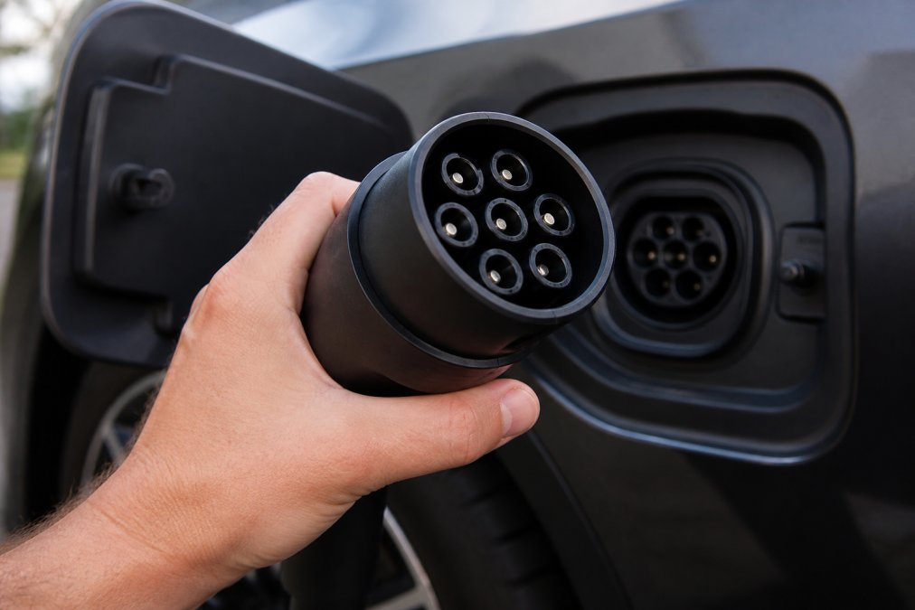 Ar roku pārbauda elektroautomobiļa 2. tipa kontaktdakšu, koncentrējoties uz metāla kontaktiem un savienojuma punktiem dabiskā apgaismojumā.