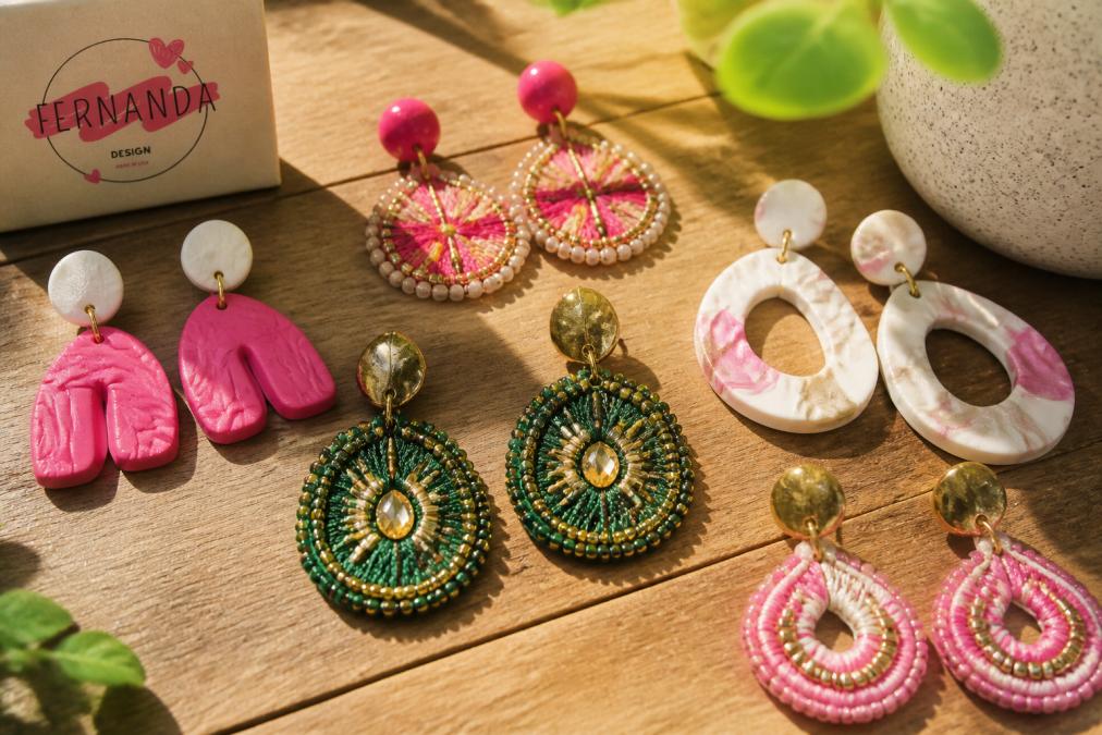 Close-up of colorful handcrafted polymer clay earrings and embroidered jewelry pieces arranged on a natural wooden surface, showcasing vibrant fuchsia, emerald green, and pearly tones with intricate beadwork and metallic details catching natural sunlight