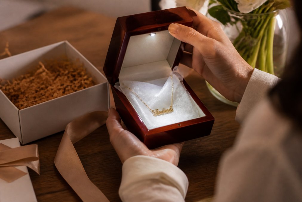 Hands opening a luxury mahogany gift box with an LED light revealing a personalized necklace on tissue paper