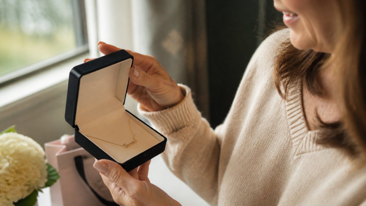 A mother opening a jewelry box to reveal a delicate personalized name necklace in soft window light