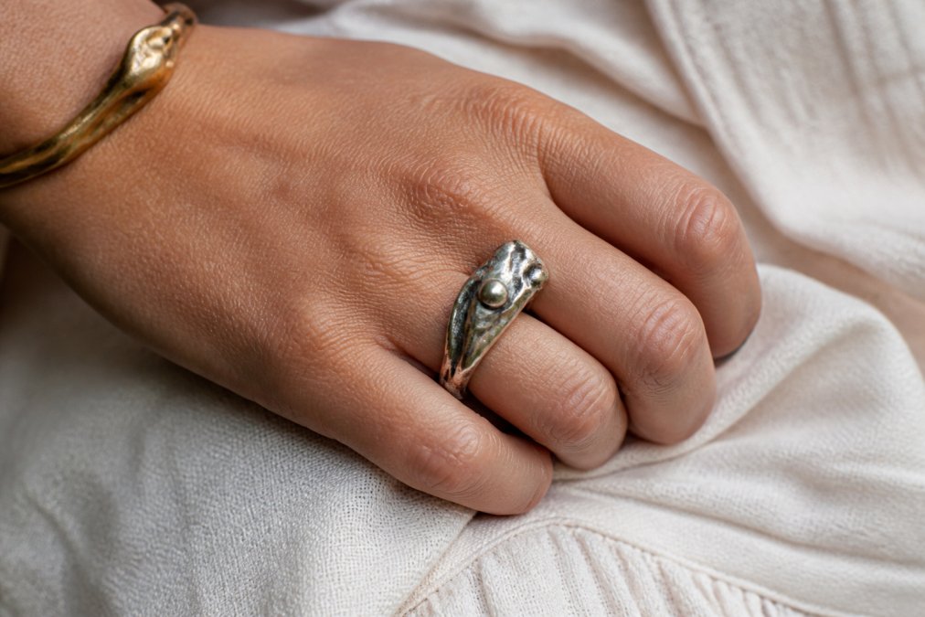 Close-up of a handcrafted fine silver ring on a person's hand, showing sculptural detail and organic patina with soft natural light highlighting the texture and craftsmanship