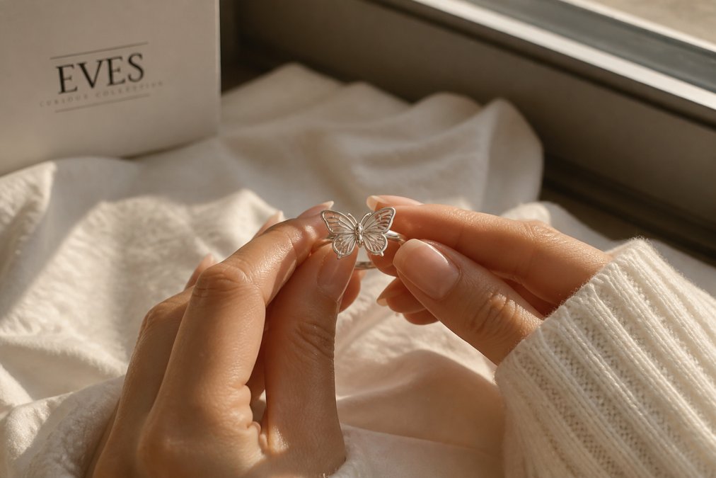 Close-up of hands holding a delicate silver butterfly ring on soft fabric, warm natural window light, shallow depth of field