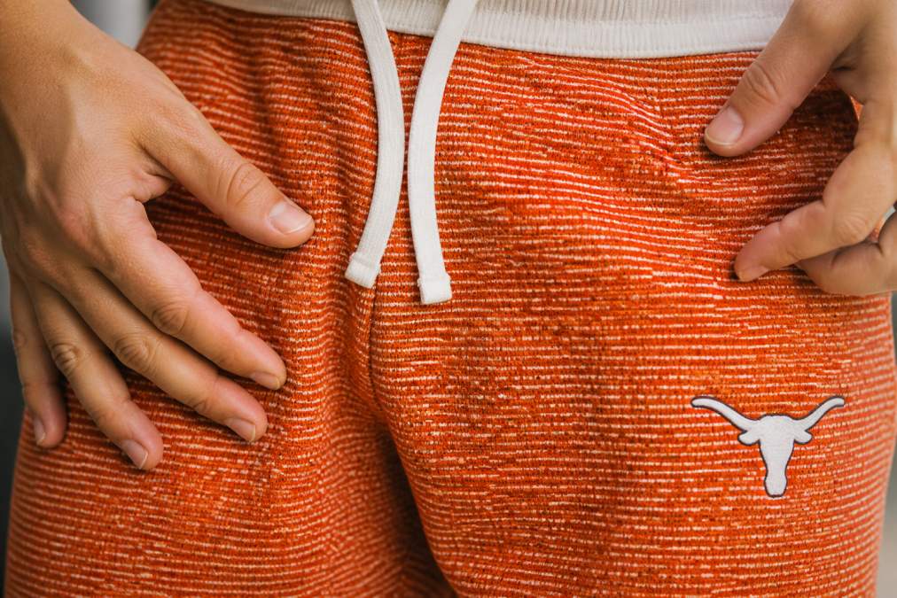 Close-up of hands running fingers across premium cotton-blend fabric showing tight weave texture under warm natural lighting, contrasted with visibly looser weave of mass-market fabric