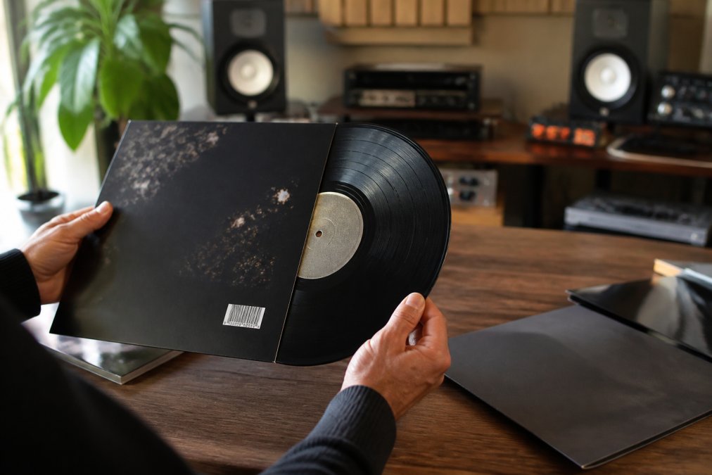 Close-up of hands holding a vinyl record and smartphone displaying music metadata and ISRC codes on screen in a bright home studio setting with professional lighting