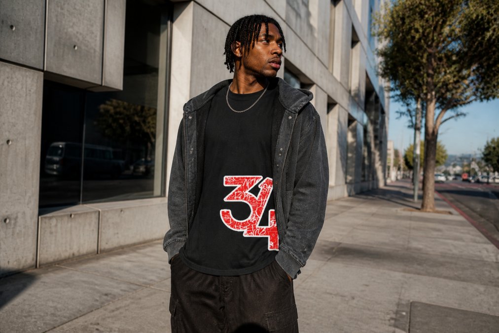 Urban tastemaker wearing oversized boxy tee with visible raw seam paneling, layered under a snow-washed snap-collar hoodie, styled with chunky white sneakers and a minimal chain necklace, standing on a modern city street with concrete architecture and natural afternoon lighting