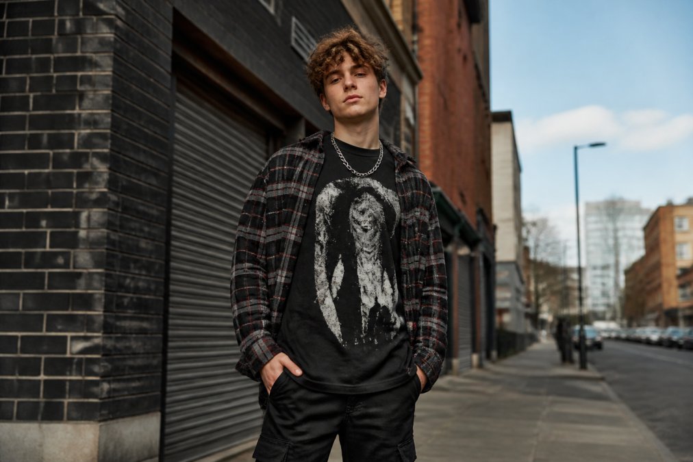 Person wearing an oversized urban graphic apparel tee layered under a flannel shirt on a city street