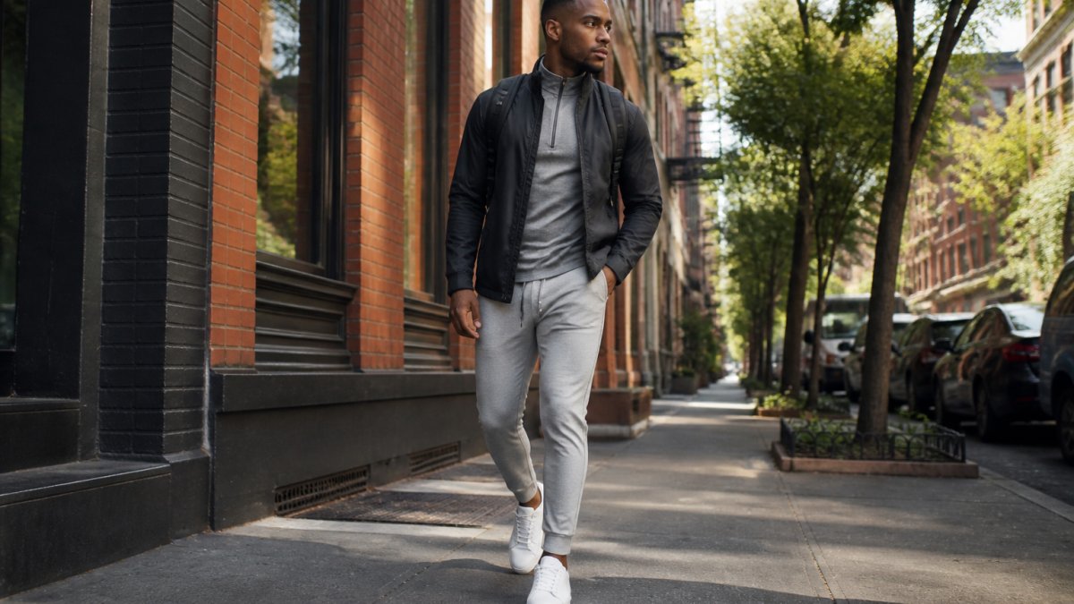 Man in neutral joggers and a technical jacket walking through a historic city street in urban hiking outfits