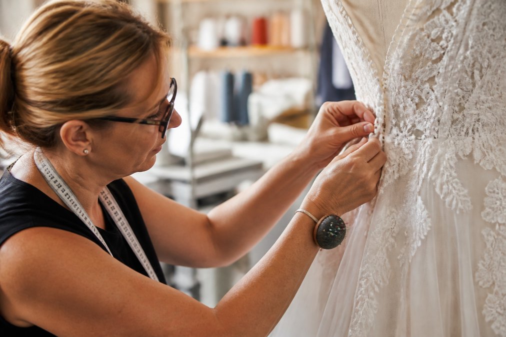 Close-up of a skilled seamstress's hands working with precision on a delicate wedding dress, carefully adjusting seams and stitching intricate alterations on white fabric with careful attention to detail