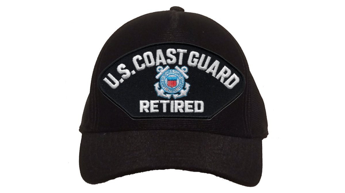 A retired Coast Guard veteran in a navy blue cap standing on a wooden dock at sunrise, holding a coffee mug and looking out at calm water