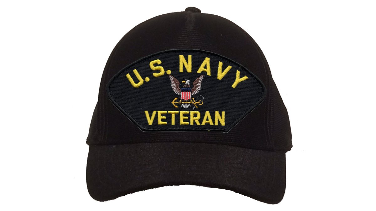 A veteran in civilian clothes trying on a navy blue embroidered veteran cap outdoors, with a subtle American flag patch visible in the background