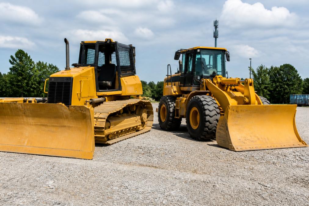 Equipment yard displaying a tracked crawler dozer positioned next to a wheeled dozer, both parked on gravel surface with clear visibility of their undercarriage and tire systems
