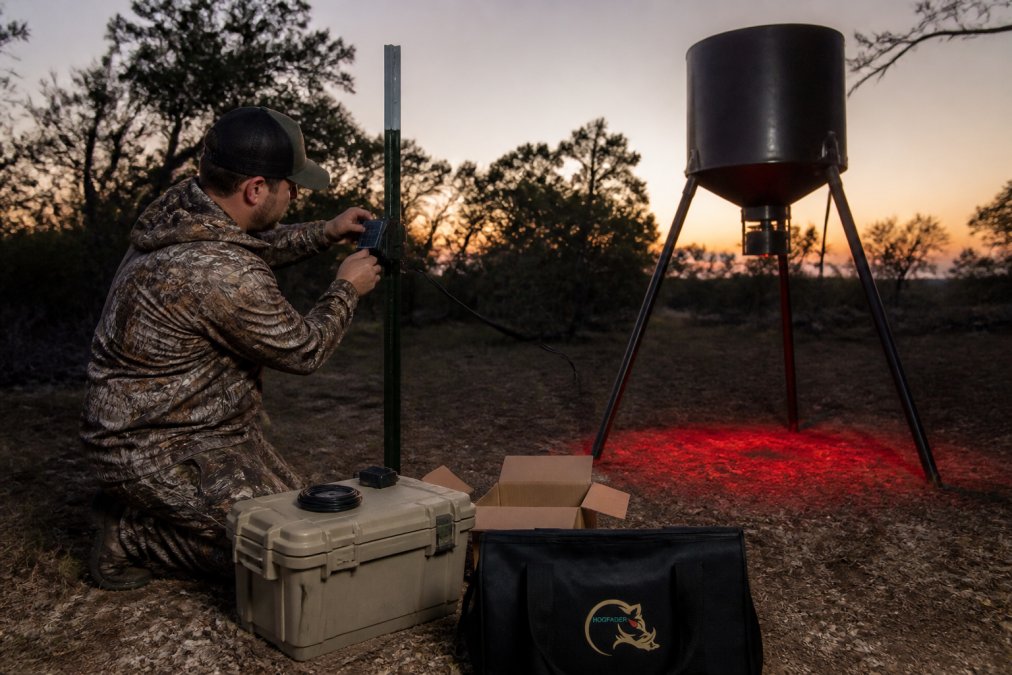 Hunter mounting solar-powered motion activated lights on a T-post by a spin feeder at dusk