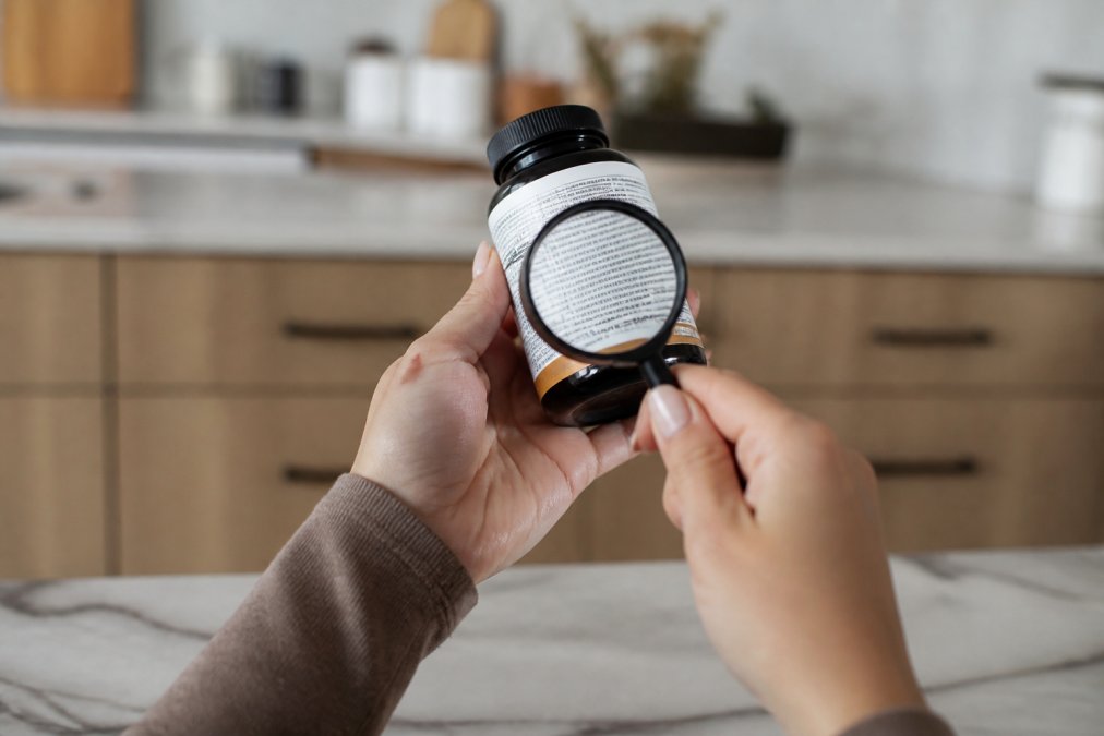 Person in a bright kitchen using a magnifying glass to check a supplement label for a USP verified seal.