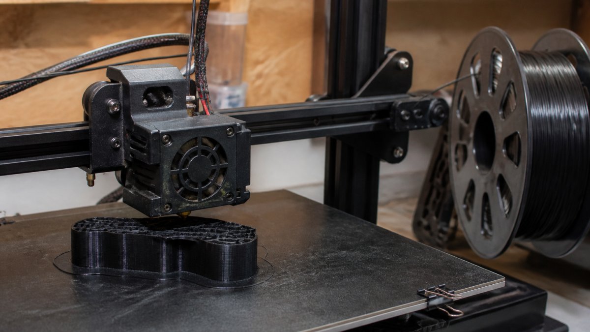 A 3D printer nozzle depositing flexible filament onto a custom holster build plate in a workshop