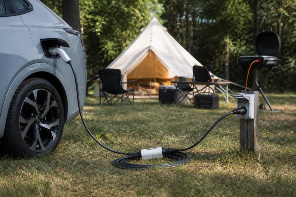 Elbil parkeret på campingplads med V2L-adapter tilsluttet strømstik til campingudstyr i dagslys