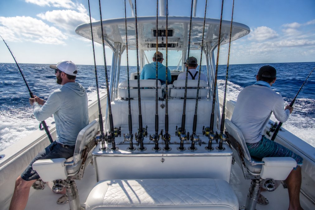A tournament fishing setup on a center console with experienced anglers at the helm and in fishing chairs, showing the deck layout, rod storage, and ergonomic console design under clear offshore conditions