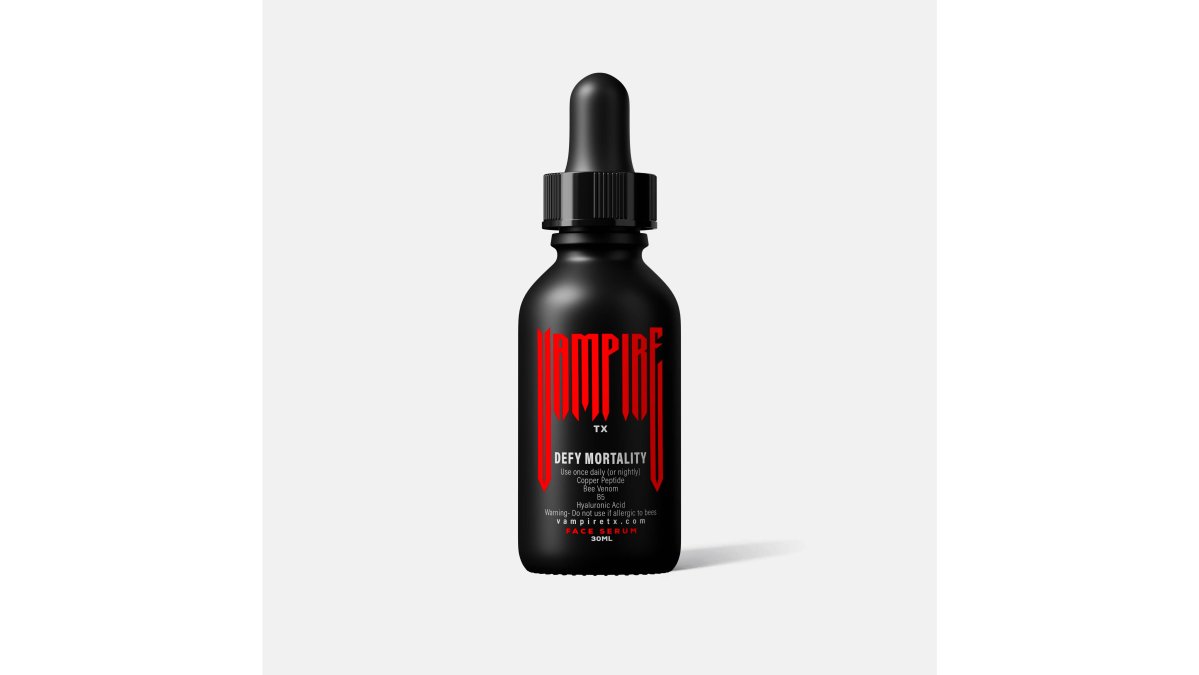 A hand holding a small glass serum bottle with an amber dropper over a clean white bathroom counter, soft natural window light falling across the skin