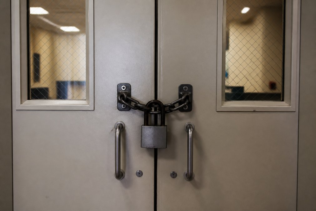 Security screening checkpoint at courthouse entrance with metal detectors, security officers checking visitor belongings, and directional signage in professional courthouse setting with fluorescent lighting