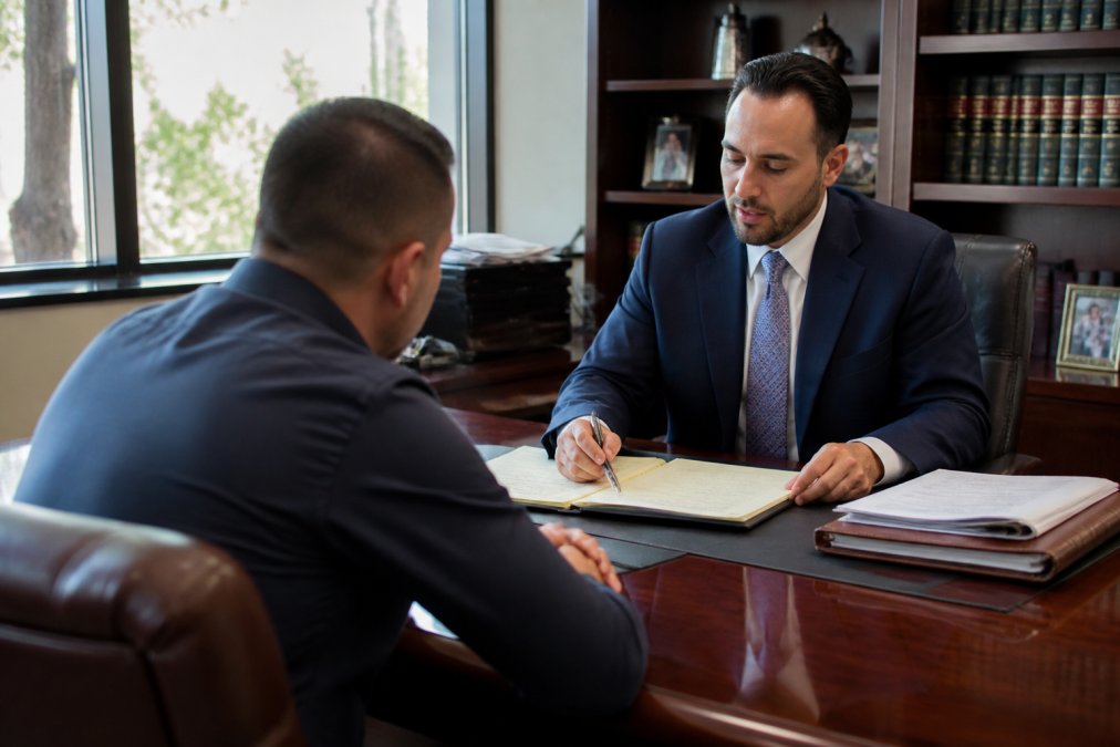 Professional criminal defense attorney in business attire meeting with a client in a modern law office consultation room, reviewing case documents and legal briefs on a polished desk with natural window lighting