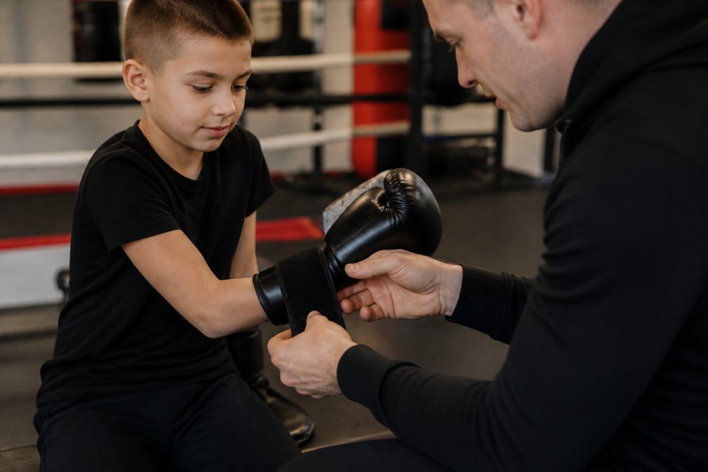 Kind van ongeveer 8 jaar dat bokshandschoenen aantrekt met hulp van een trainer, close-up van de pasvorm rond de pols en hand