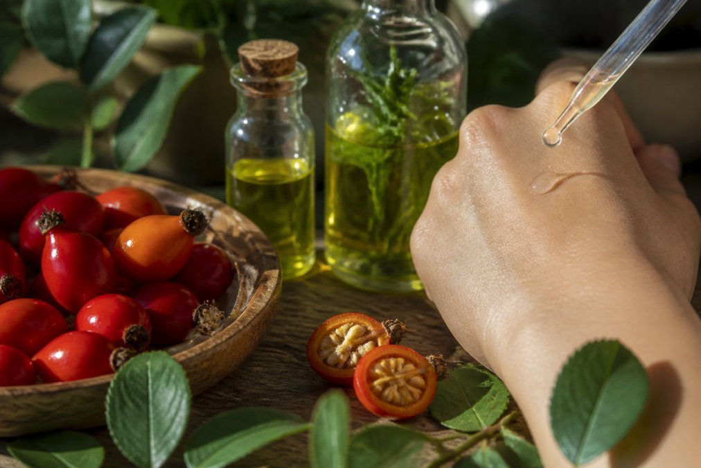 Close-up of botanical ingredients including fresh rosehip berries, hyaluronic acid serum droplets glistening on skin, and green plant extracts in glass bottles arranged on natural wooden surface with soft morning light