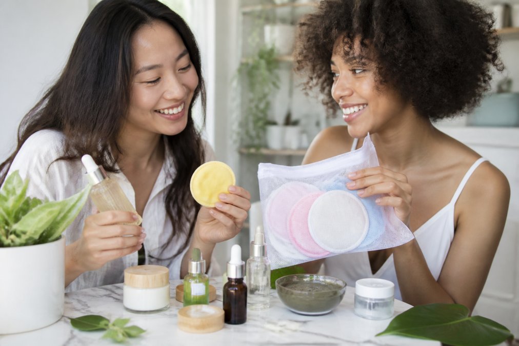 Flat lay of vegan skincare trial products arranged on a marble surface with glass bottles of serums, cream masks, and bamboo makeup remover pads, surrounded by fresh green botanical leaves and morning sunlight