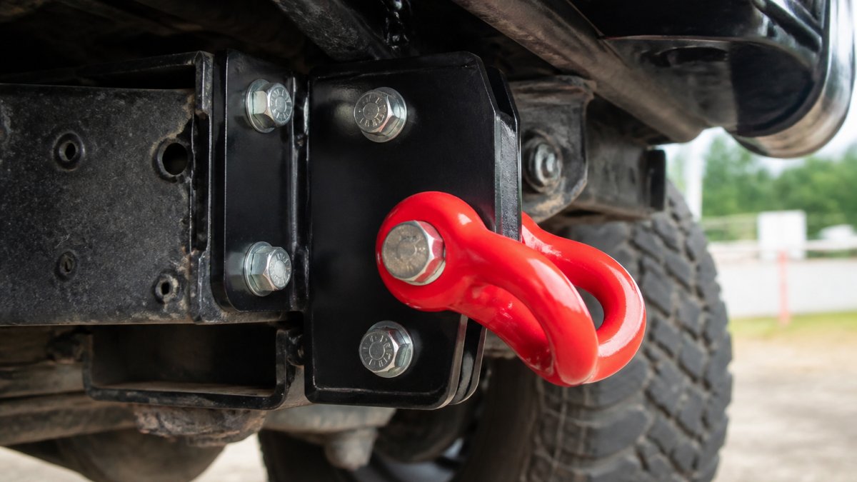 Close-up of a rated recovery point bolted securely to a vehicle chassis, showing the reinforced mounting bracket, heavy-duty fasteners, and structural attachment to the frame
