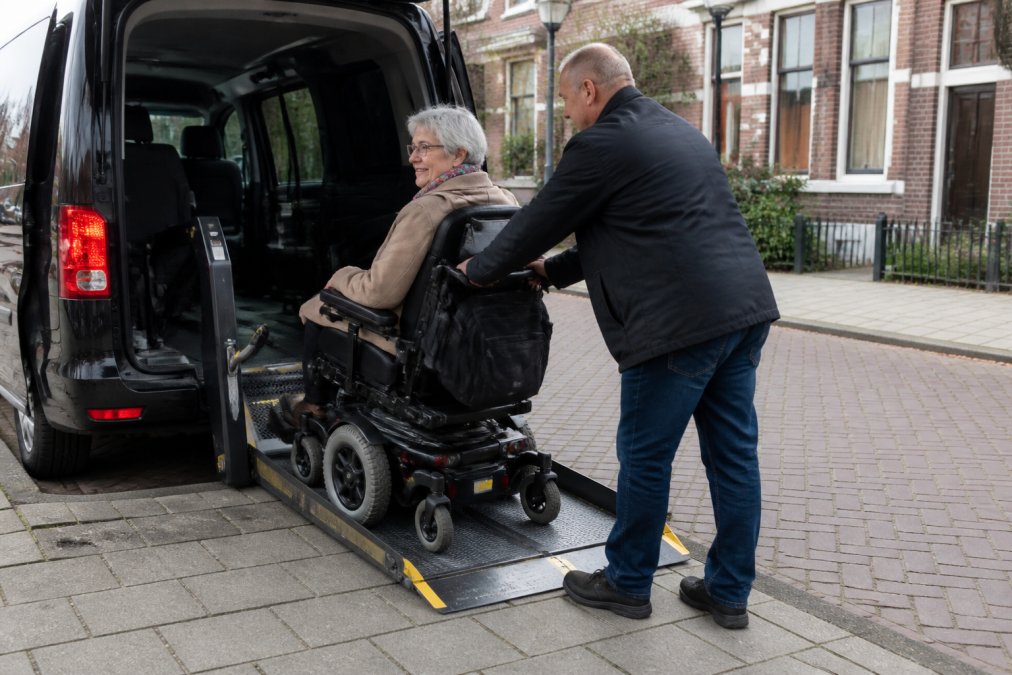 Chauffeur helpt oudere dame veilig in en uitstappen rolstoel via de lift van een aangepast voertuig