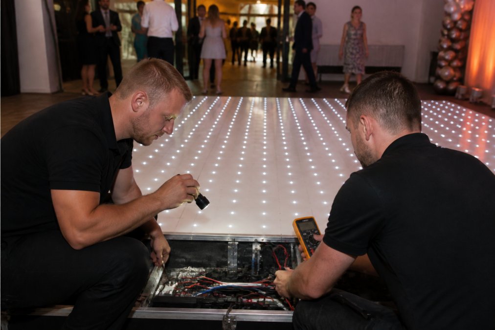 Medewerkers controleren de bekabeling van een verlichte dansvloer met een multimeter voor aanvang van een feest