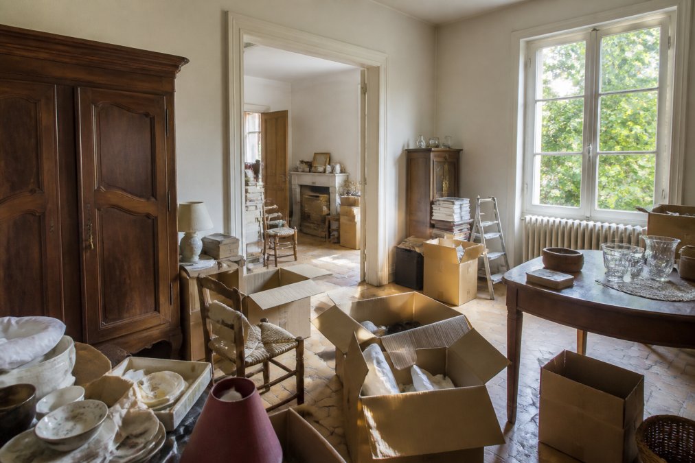 Intérieur d'une maison ancienne en cours de vide avec des cartons, meubles et objets à trier, montrant le travail de désencombrement dans la lumière naturelle