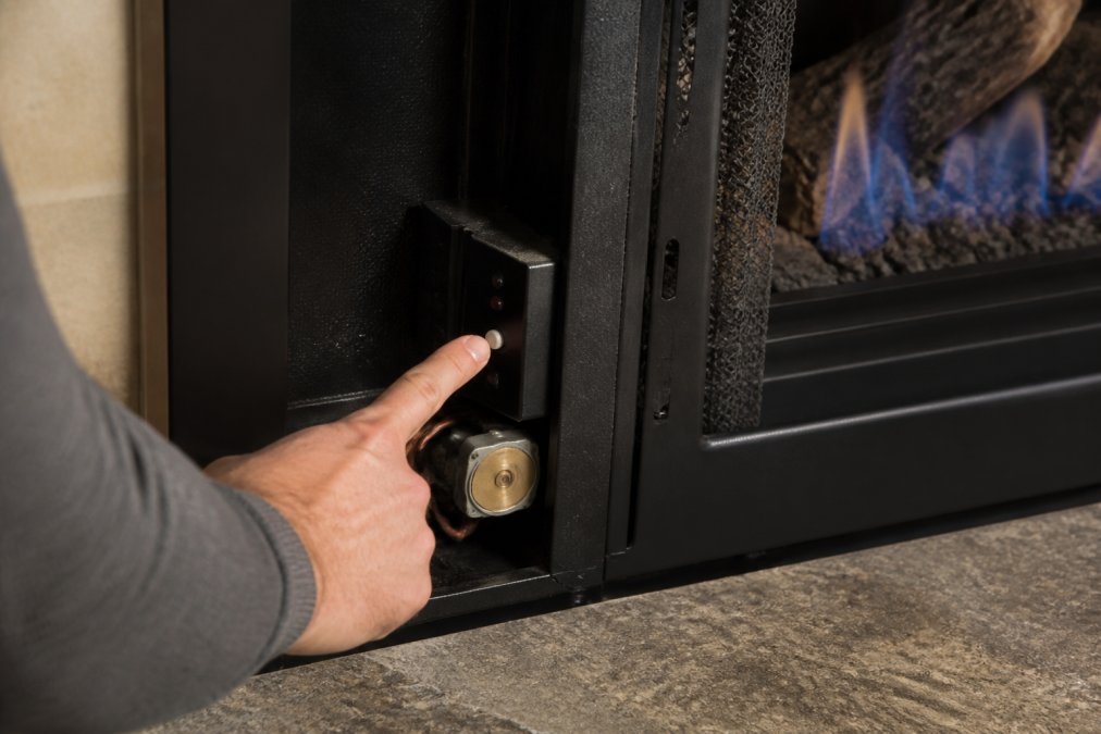 Close-up of a homeowner's hand pointing to the oxygen depletion sensor control panel inside a modern ventless gas fireplace, with blue flames visible in the background