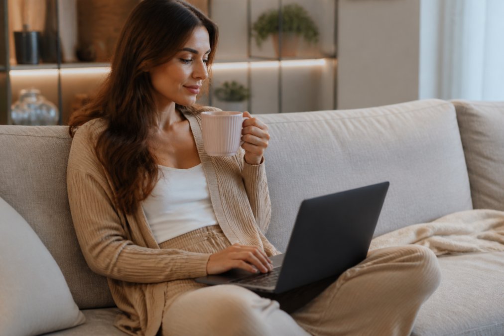Persoon zittend in een comfortabele thuisomgeving op een bank met een laptop, ontspannen aan het bladeren door een webshop met een kopje thee, wat vertrouwen en privacy symboliseert