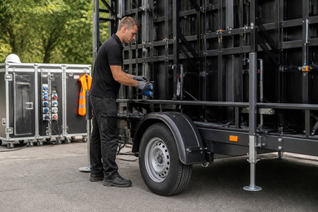 Professionele technicus die een mobiel LED-scherm op een aanhangwagen opstelt, met zichtbare elektriciteitskasten en veiligheidsuitrusting op de achtergrond