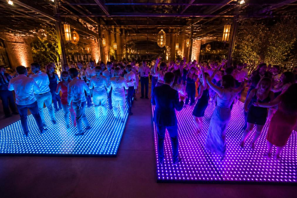 Twee groepen gasten dansend op twee verschillende maten verlichte dansvloeren (een kleinere 4x4m en een grotere 8x6m) naast elkaar, beide vol met dansende mensen in feestelijke kleding, LED-effecten in blauw en paars