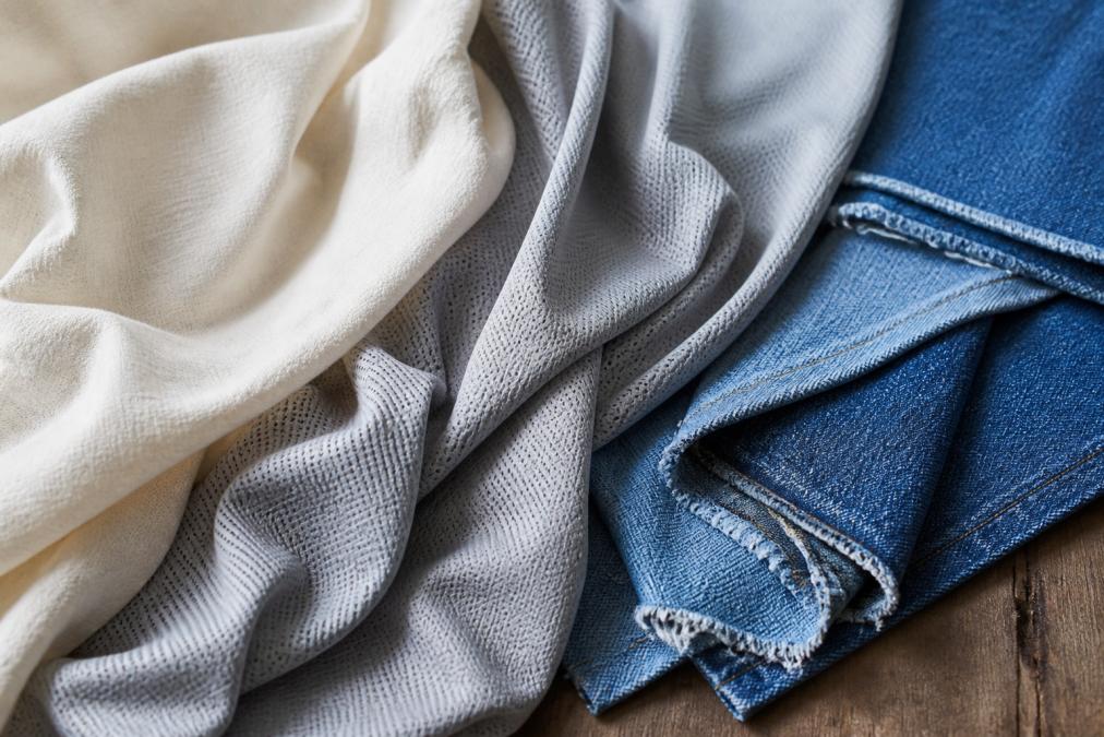 Close-up of various fabric textures arranged to show breathable cotton, stretchy performance polyester blend, and durable denim swatches with natural daylight highlighting their weave patterns