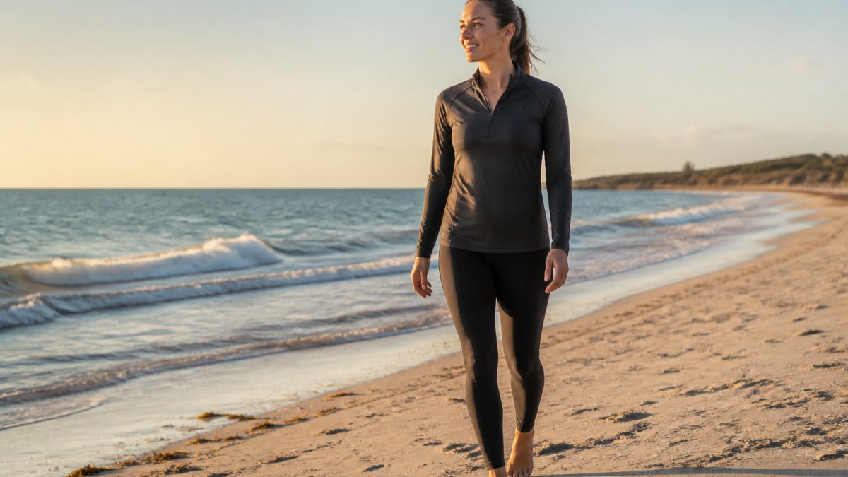 A woman wearing UPF 50+ swim leggings walking on a sandy beach at golden hour, gentle waves behind her, relaxed and confident posture