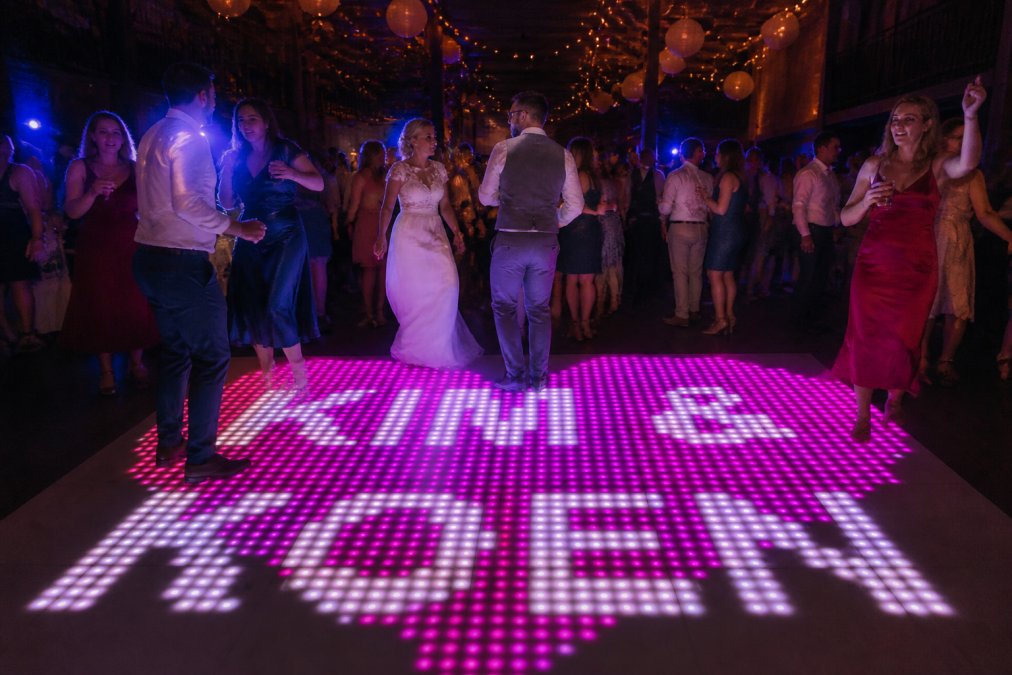 Groep gasten dansend op een spectaculaire verlichte pixeldansvloer op een bruiloft, met dynamische animaties en kleurrijke effecten zichtbaar onder hun voeten