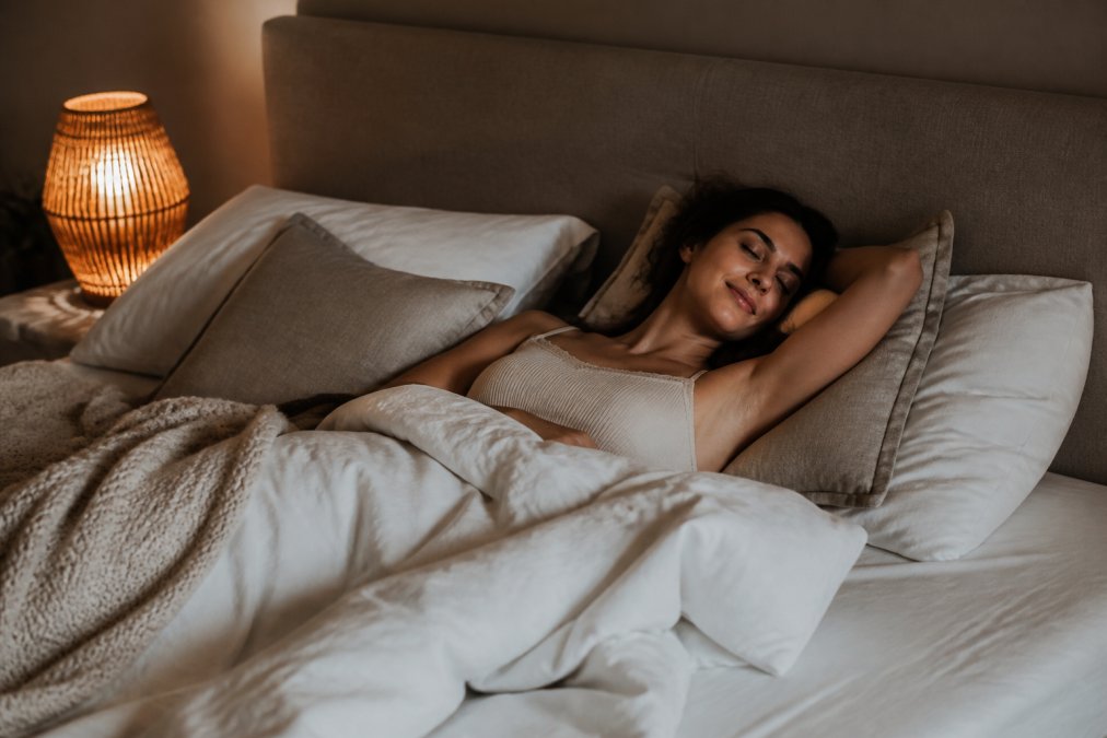 Rustige slaapkamer met zachte, warme verlichting, comfortabel bed met kussens en dekens, een persoon in ontspannen houding liggend