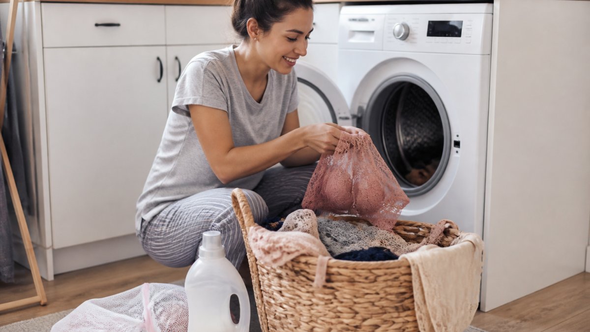 A flat-lay photograph of several lace bralettes and bra sets in neutral tones arranged on a clean white surface, with a small mesh laundry bag and gentle detergent bottle beside them, suggesting careful washing and garment care
