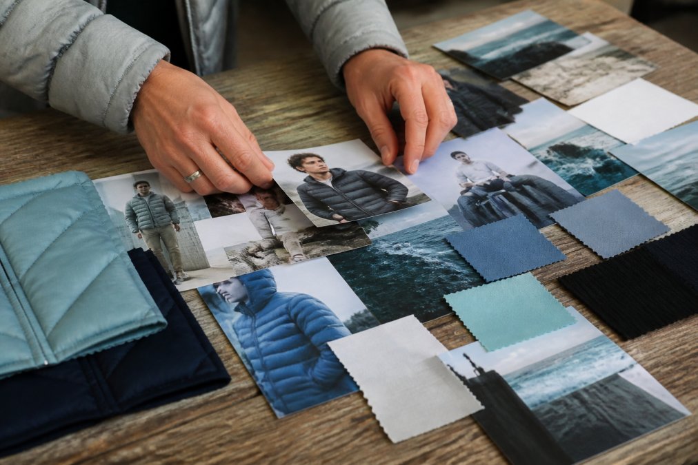 Close-up van handen die gedrukte mode-inspiratiebeelden, kleurstalen en stoffen samples op een houten oppervlak rangschikken om een moodboard samen te stellen