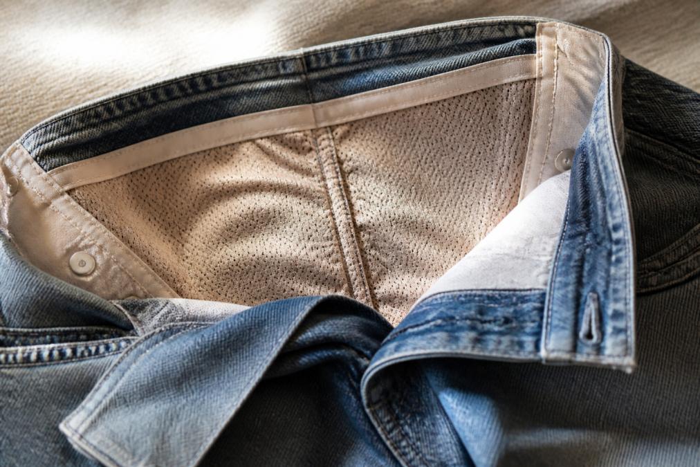 Close-up detail shot of the inner waistband construction showing the mesh panel and compression technology in premium vintage jeans, with soft natural lighting highlighting the hidden support system that provides midsection smoothing
