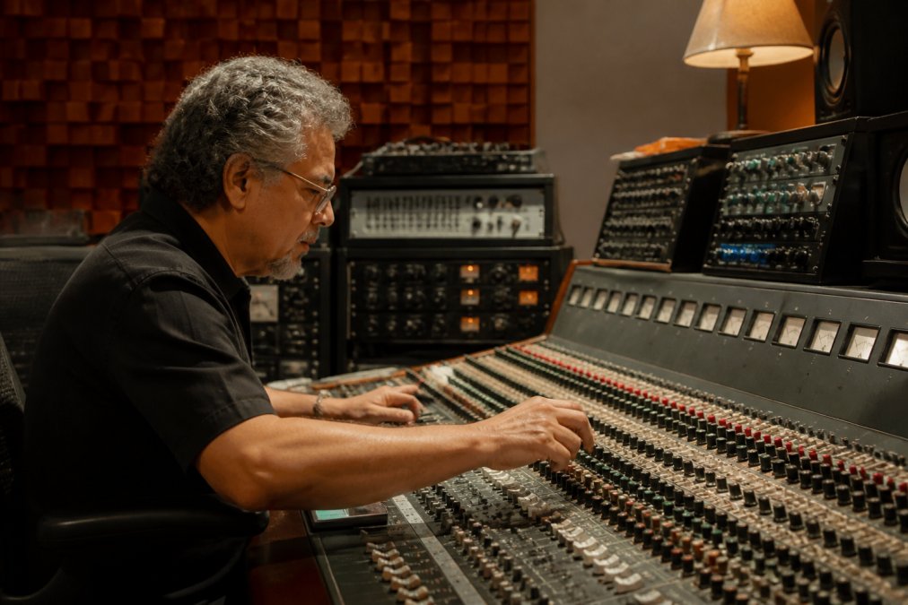 Close-up of a mastering engineer's hands adjusting controls on a vintage analog console, surrounded by outboard gear, in an acoustically treated studio with warm ambient lighting