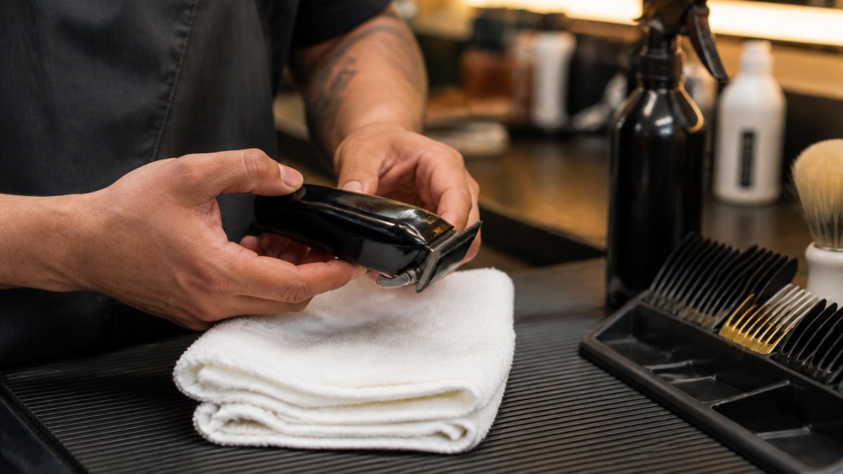 Barber adjusting the taper lever on a cordless clipper over a white towel in a warm, professional shop setting