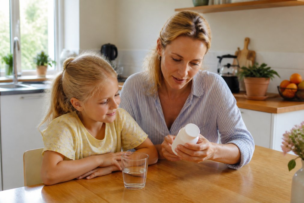 Infografik der viser processen for valg af sunde vitaminer til børn i et lyst køkkenmiljø med vandglas.