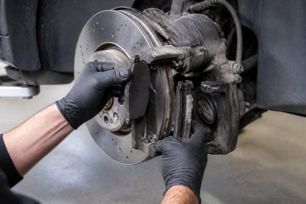 Professional technician's hands working on Volkswagen Golf R Mk7 brake caliper and rotor assembly, showing brake pad removal and component inspection in detail during installation